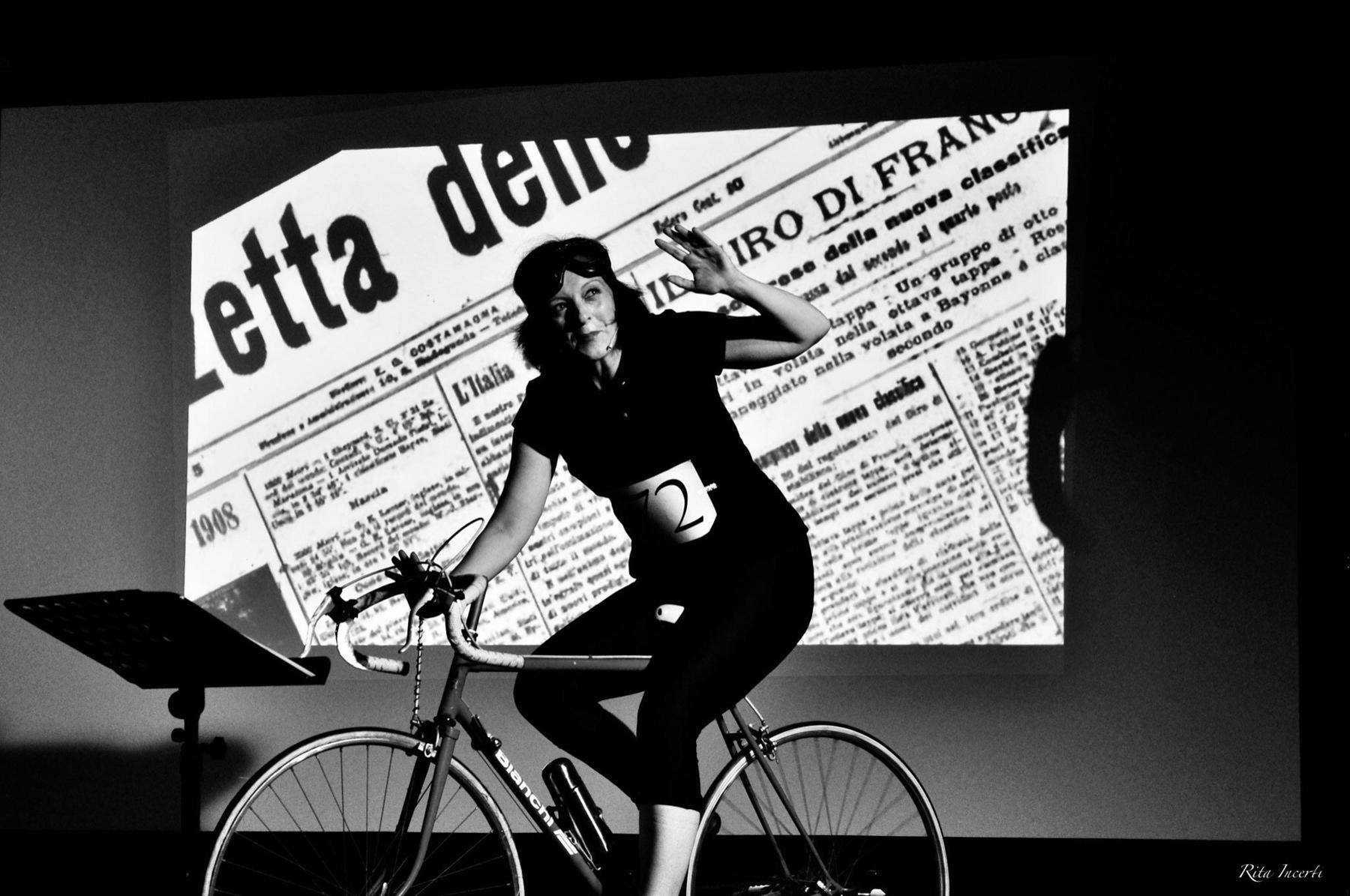 Maria Giulia Campioli interpreta Alfonsina Strada in bicicletta, davanti alla proiezione di un giornale d’epoca.